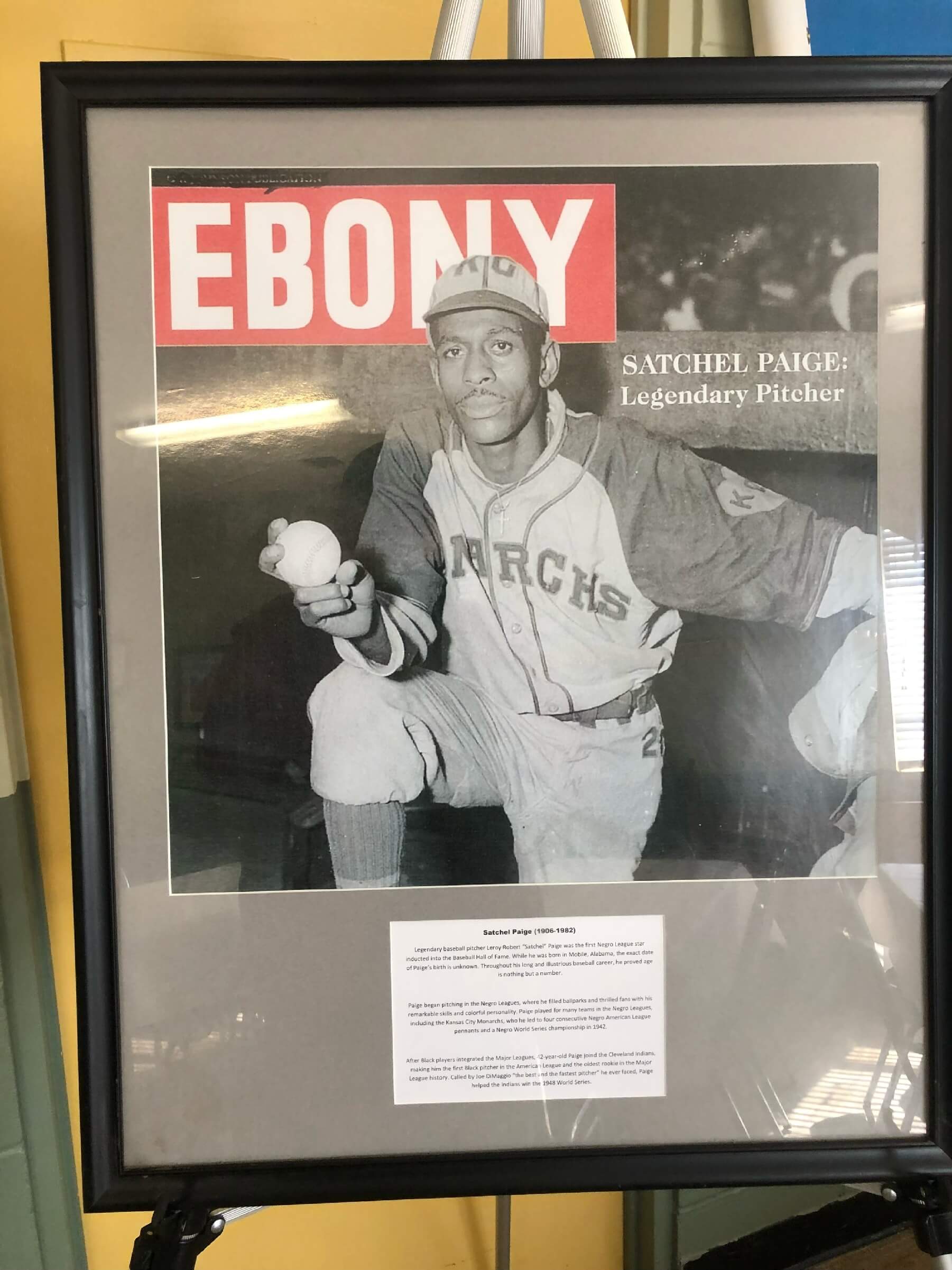 A framed Ebony magazine cover featuring a black-and-white photo of legendary pitcher Satchel Paige in his Kansas City Monarchs uniform.