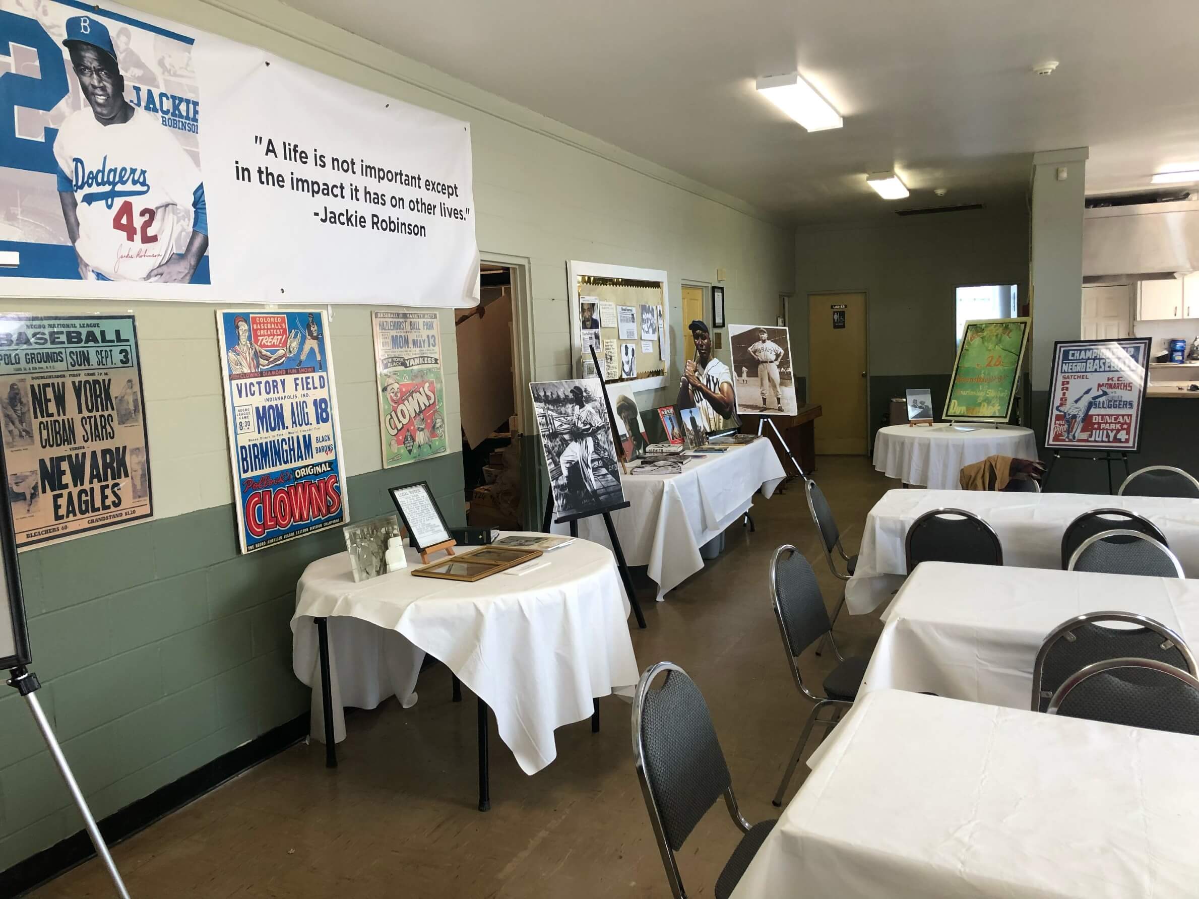 A room set up for an event with white-clothed tables and a museum-style display of Negro League baseball posters and a Jackie Robinson banner.