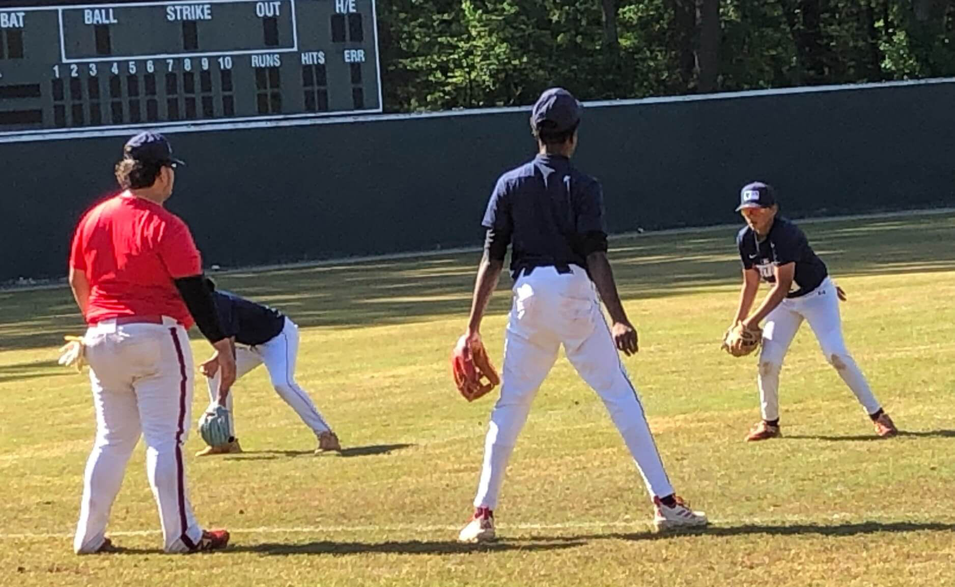 A coach in a red jersey instructs young infielders in fielding stance during the Palmetto Baseball Prospects clinic at Duncan Park Stadium